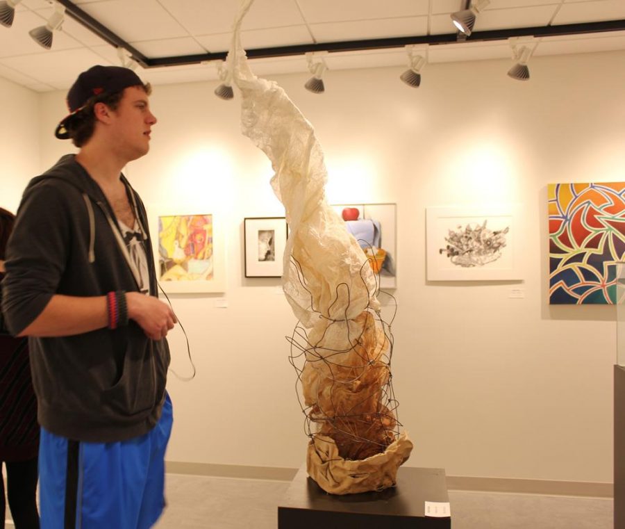 Wayne State student Justin Stanton browses the gallery, standing next to a tall piece of art created by Halie Holton.