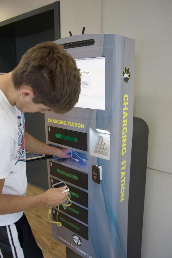 Tyler+Lutt+uses+the+charging+station+in+the+library+to+charge+his+phone.