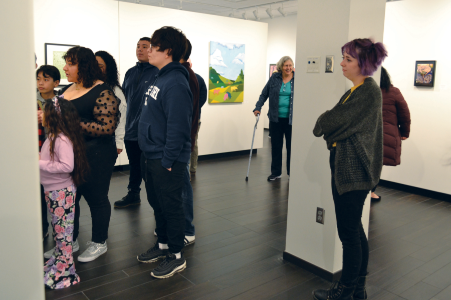 A group of people visiting the senior art exhibit, titled Roots and Routes, in the Nordstrand Visual Arts Gallery in the Conn Library.